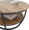 A round coffee table with a wooden top and black metal legs, featuring a lower shelf with a white box on it. Headphones and papers are on the top surface. Produktbild-Vorschau