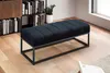 A black upholstered bench with a metal frame sits on a wooden floor in a room with bookshelves and a window. Podgląd zdjęcia produktu