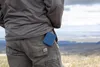 A person's back pocket with a blue silicone cutlery holder sticking out, with a scenic landscape in the background. Produktbild-Vorschau