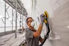 A person is sanding a large white surface, likely a boat or vehicle, indoors with scaffolding and lights in the background. Produktbild-Vorschau