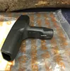 A black T-handle tool is shown on a clear plastic bag with orange markings. A piece of wood is visible in the background. Produktbild-Vorschau