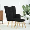A black fabric armchair and ottoman are shown in a well-lit room with a large plant and a floor lamp in the background. Anteprima dell’immagine prodotto