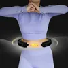 A person wearing athletic clothing is shown from the waist down, with a massage hula hoop around their waist. The hoop has glowing yellow elements, suggesting it is active or has features. Náhled obrázku produktu