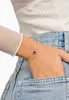 A person's hand wearing a bracelet with a red stone, with their hand in the pocket of their jeans. Podgląd zdjęcia produktu