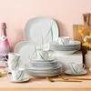 A collection of white dinnerware with green accents, including plates, bowls, cups, and saucers, arranged on a wooden surface with a pink background. A bottle of pink sparkling wine is also visible. Náhled obrázku produktu