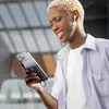 A young man with blonde hair is looking at his phone, which is attached to a power bank. Produktbild-Vorschau