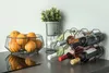 A wine rack with six bottles of wine and a fruit basket filled with oranges are displayed on a countertop. Náhled obrázku produktu