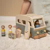A child's hand is visible, playing with a wooden toy camper van and accessories on a fluffy rug. Náhled obrázku produktu