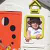 A young boy wearing a hat peeks out of a window of a playhouse. Produktbild-Vorschau