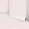 A close-up view of a white flexible baseboard molding installed along a curved wall and a straight wall in a room with light pink walls and floor. Anteprima dell’immagine prodotto