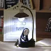 A decorative lamp featuring a character from Japanese animation, placed on a shelf with books and a photo frame. Produktbild-Vorschau