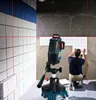 A person is tiling a wall with the help of a laser level. Voir les images du produit
