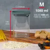A glass storage jar with a lid, placed on a wooden board with dried fruits, nuts, and pasta. Dimensions and capacity are indicated with text overlays. Produktbild-Vorschau