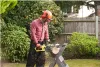 A man is using an electric chainsaw to cut a log in a garden. Anteprima dell’immagine prodotto
