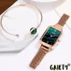 A rose gold watch with a green dial and a matching mesh band is displayed next to a rose gold bangle with a green stone. Produktbild-Vorschau