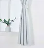 A light gray curtain is tied back with a fabric band, hanging next to a window. A white vase with green leaves sits on the windowsill. Produktbild-Vorschau