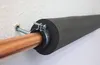 A copper pipe is insulated with black foam and secured with a clamp to a white wall. Produktbild-Vorschau