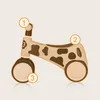 A balance bike with a cow pattern, featuring numbered callouts. Anteprima dell’immagine prodotto