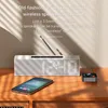 A smartphone and a wireless audio adapter are placed on a wooden table in front of a silver speaker with a digital clock display. Podgląd zdjęcia produktu