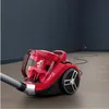 A red vacuum cleaner is shown in a room with dark gray walls and a wooden floor. Voir les images du produit