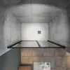 A top-down view of a modern shower enclosure with glass doors and black metal framing, set against tiled walls and floor. Produktbild-Vorschau