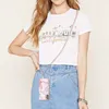 A woman wearing a white t-shirt and denim skirt, holding a phone with a lanyard. Náhled obrázku produktu