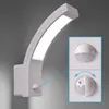 A white LED outdoor wall light with a curved design is mounted on a gray wall. An inset shows a close-up of the motion sensor, with one image showing it in its standard state and another showing it with adjustable settings indicated by arrows. Produktbild-Vorschau