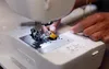 A close-up shot of a person's hands using a white Brother sewing machine. Produktbild-Vorschau