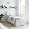 A white upholstered bed with a mattress and a throw blanket is shown in a bright, minimalist bedroom setting. Produktbild-Vorschau