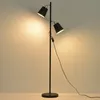 A black and gold two-headed floor lamp is shown against a light gray background. Náhled obrázku produktu