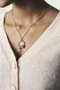 A person wearing a light pink cardigan and a silver necklace with a pendant. Podgląd zdjęcia produktu