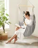 A woman is relaxing in a hanging chair, reading a book and holding a mug. Náhled obrázku produktu