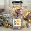 A glass jar filled with round, brown candies, tied with a gold ribbon and decorated with a Christmas-themed gift tag. Produktbild-Vorschau