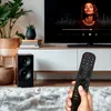A hand holding a remote control in front of a TV and entertainment center. Voir les images du produit