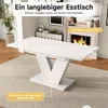A white extendable dining table with a V-shaped base is shown in a well-lit room with a fireplace in the background. Anteprima dell’immagine prodotto