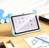 A child's tablet with blue ear-like protectors is placed on a wooden desk next to a drawing and a blue toy. Náhľad obrázku produktu