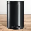 A black pedal trash can is shown on a wooden floor against a white wall. Podgląd zdjęcia produktu