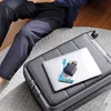 A person sitting on the floor next to a suitcase, with a laptop, charger, and ticket on top of the suitcase. Produktbild-Vorschau
