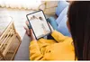A person is holding a tablet, looking at a screen that displays a woman reaching for something on a shelf. Produktbild-Vorschau