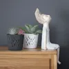 Two decorative planters with air plants and a small figurine sit on a wooden surface against a gray wall. Voir les images du produit