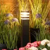 A garden setting with a black bollard light surrounded by tall grasses and purple flowers, with pink and white flowers in the foreground. Anteprima dell’immagine prodotto