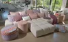 A living room scene with a large sectional sofa and decorative pillows, with a round ottoman in the foreground. Produktbild-Vorschau