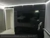 A modern living room with a large TV mounted on a dark gray upholstered wall. Produktbild-Vorschau