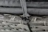 A close-up view of a gray woven outdoor furniture piece with cushions and a tie-down strap with a toggle. Produktbild-Vorschau