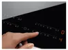 A close-up of a finger interacting with the touch controls of a black induction cooktop. Podgląd zdjęcia produktu