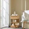 A wooden nightstand with decorative items next to a window with sheer curtains and a white sofa. Produktbild-Vorschau