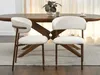 Two beige upholstered dining chairs with walnut legs are placed in front of a wooden dining table. Voir les images du produit