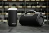 Two black Bluetooth speakers are placed on a dark surface, with shelves of black objects in the background. Anteprima dell’immagine prodotto