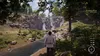 A person stands on a path next to a river, looking towards a waterfall in a forest setting. Náhled obrázku produktu