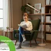 A woman is reading a book while sitting in a green armchair, with a floor lamp providing light. Anteprima dell’immagine prodotto